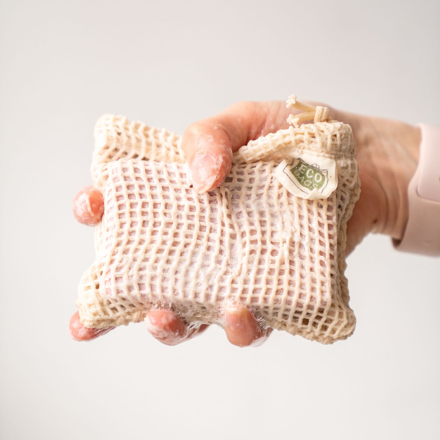 A hand holds a soap saver bag made from natural cotton covered in soapy lather