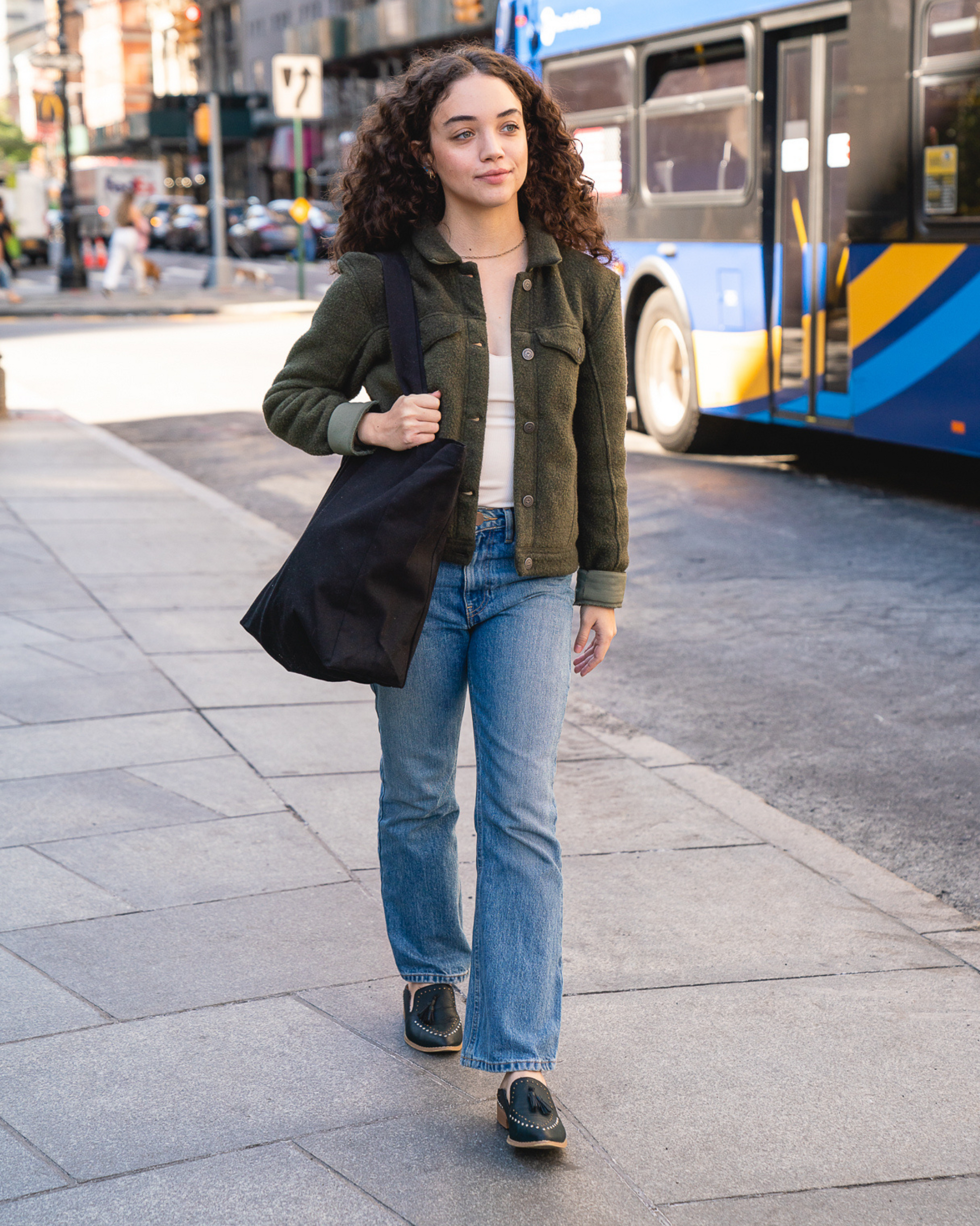 Woman walking on a city street holding a black tote bag