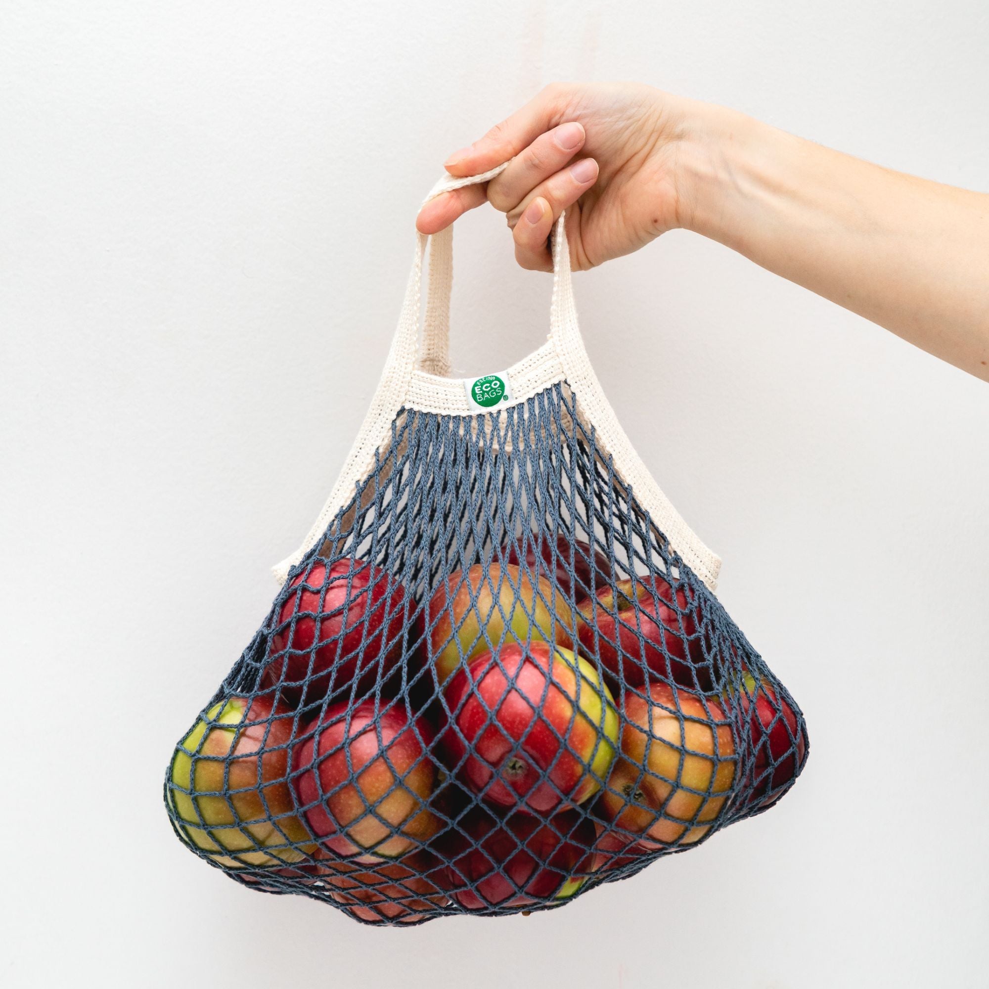 Hand holding blue and natural mini string bag filled with red apples