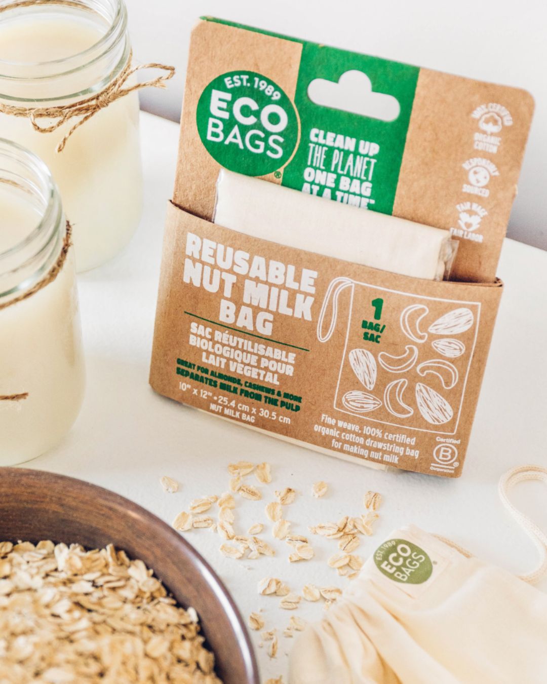 Reusable nut milk bag packaging with jars of milk and oats on a white surface