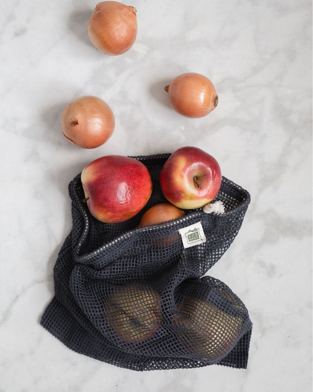 Storm blue mesh produce bag with apples and onions on a light gray background