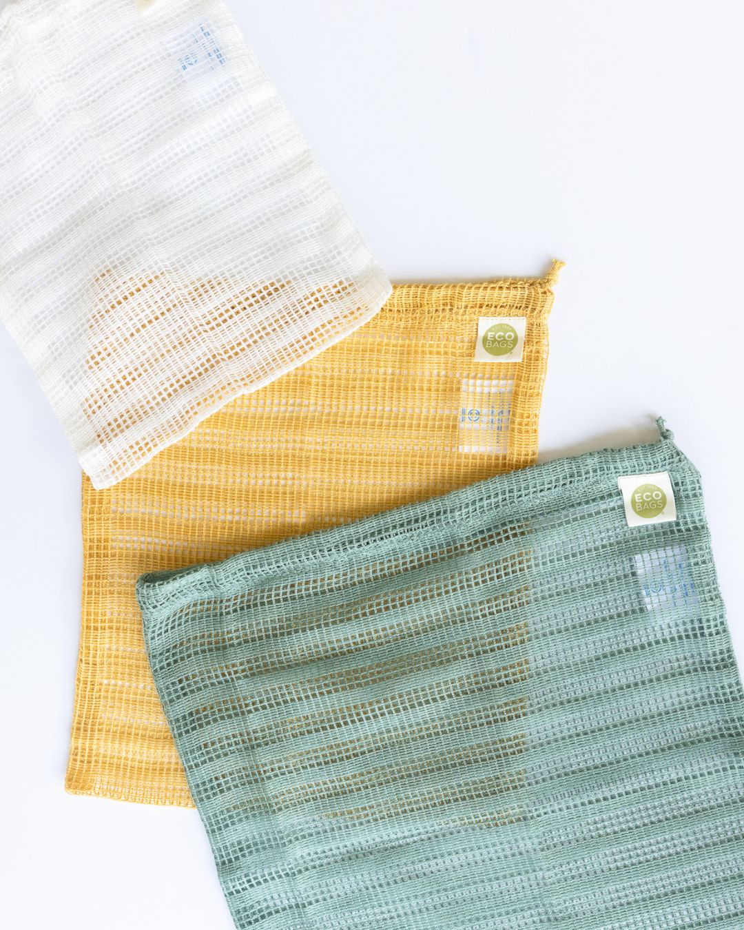 Three cellulose reusable produce bags in white, yellow, and green on a white background