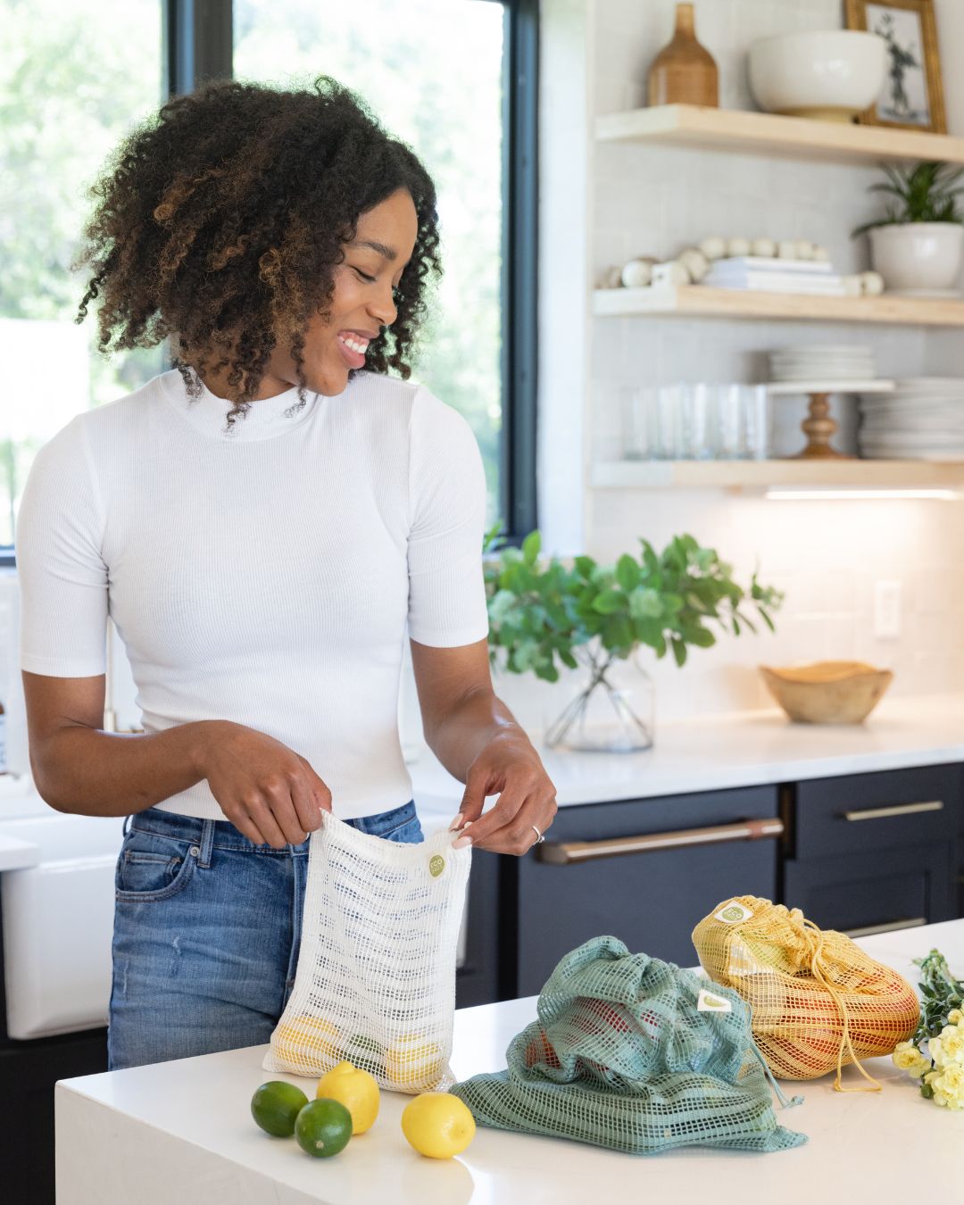 Woman in a kitchen unpacking groceries from a reusable mesh bag.