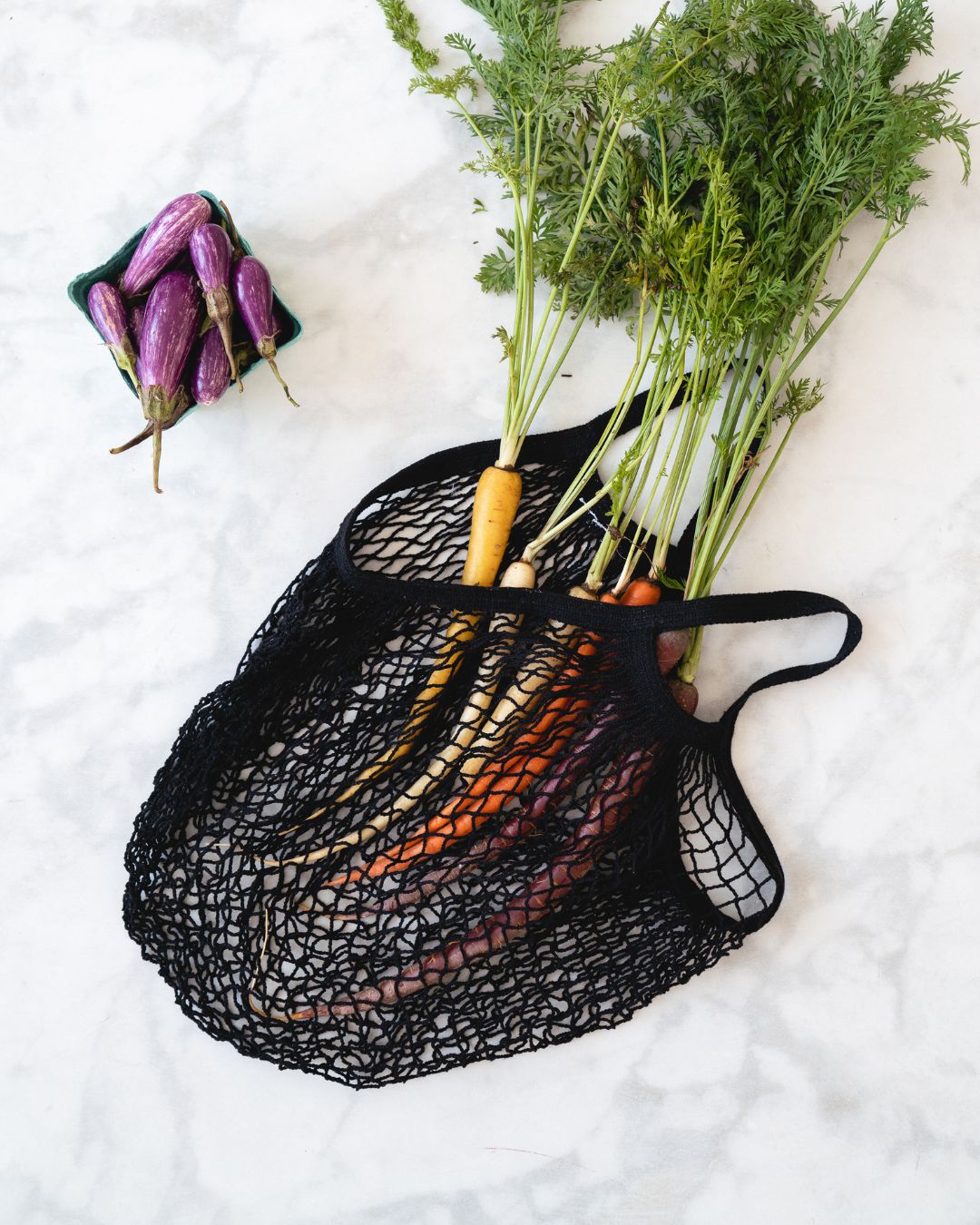 Black mesh string bag with carrots and egglplants on a white background