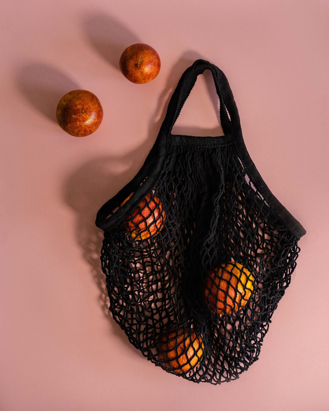 Black mesh string market bag with apples on a pink background
