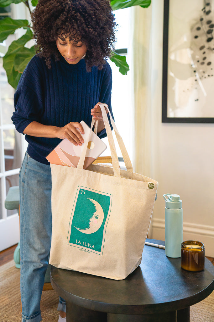 a person puts a notebook into a screen printed tote bag with a teal design