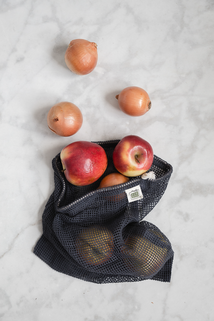 A large dark blue mesh bag holds apples and other grocery  veggies